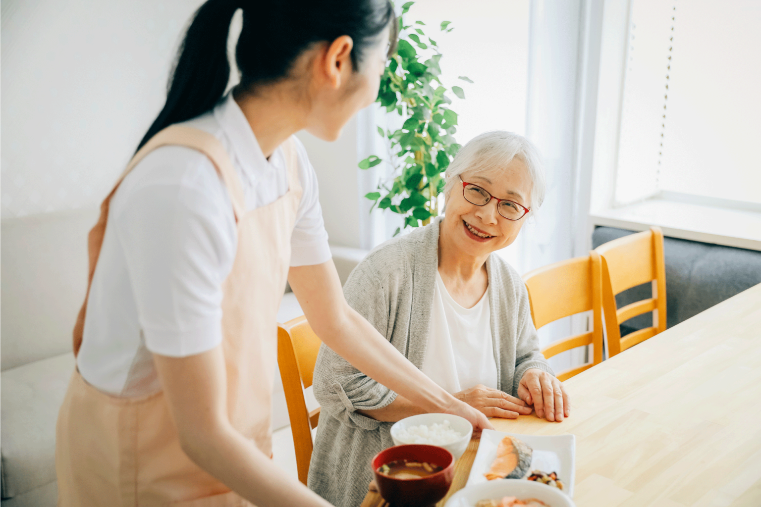 職員が高齢者と食事時間を共にしている。温かみのある交流風景。